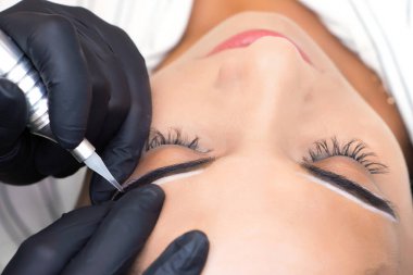 Güzellik uzmanı genç ve güzel bir kadının yüzüne kalıcı kaş makyajı yapar.