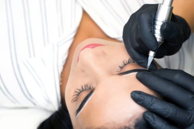 Güzellik uzmanı genç ve güzel bir kadının yüzüne kalıcı kaş makyajı yapar.