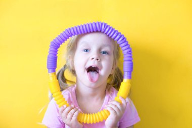 pop tüpü. Bir çocuğun elindeki pop tüpünden çıkan stres önleyici plastik oyuncak. Neşeli küçük kız oyuncak bir pop tüpüyle oynuyor. 2021 trendi. Sarı arkaplan