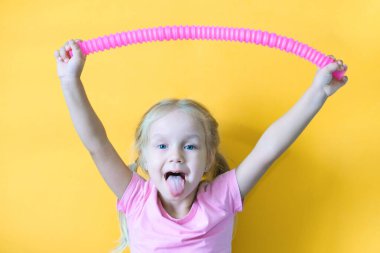 pop tüpü. Bir çocuğun elindeki pop tüpünden çıkan stres önleyici plastik oyuncak. Neşeli küçük kız oyuncak bir pop tüpüyle oynuyor. 2021 trendi. Sarı arkaplan