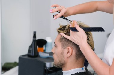 Kuaför, kuaförde sarı saçlı, makaslı genç bir adamın saçını kesiyor. Profesyonel saç bakımı..