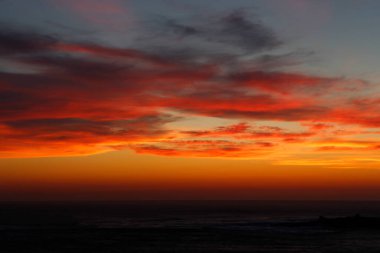 Ufukta deniz kenarında kızıl güneşle gün batımı