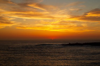 Ufukta deniz kenarında kızıl güneşle gün batımı