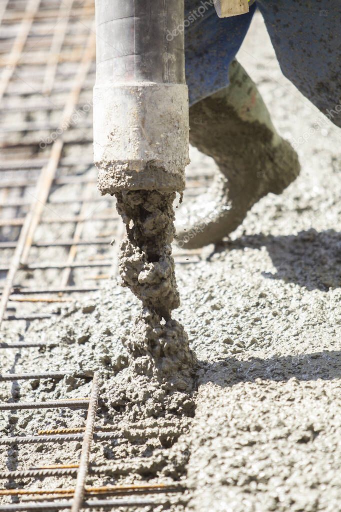 Worker filling the foundation slab of a building under construction with a pipe from which cement comes out