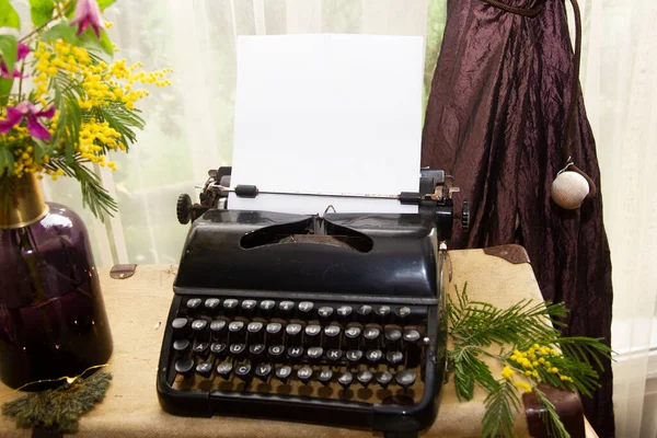 old typewriter with white folio on wooden table with floral decoration