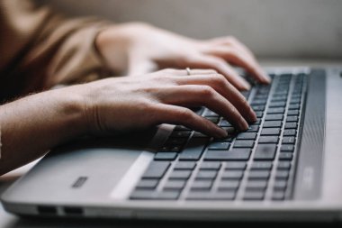 Eller beyaz ahşap bir masanın üstünde dizüstü bilgisayarda klavye kullanıyor.