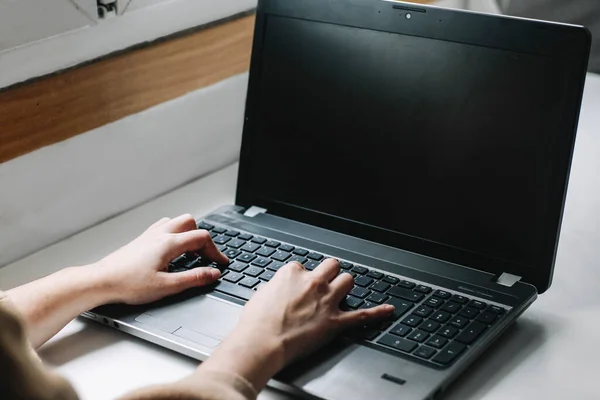 Eller beyaz ahşap bir masanın üstünde dizüstü bilgisayarda klavye kullanıyor.
