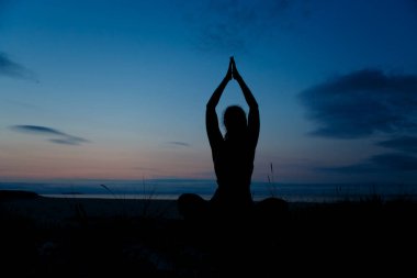 Silhouette of young woman practicing yoga, lotus position, and meditating on the beach