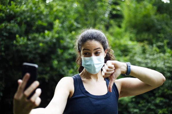 公園にはヘッドフォンとスマートフォンを持ったマスクをした若い白人女性が — ストック写真