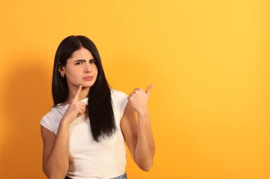 Çenesinde bir parmak, şüphe, merak ve şüphecilik göstererek ayakta duran genç bir kadın parmağını sağa doğru uzatarak bir seçim ya da yön öneriyor.