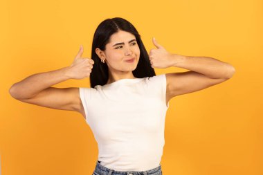 Genç bir kadın gülümsüyor ve turuncu arka planda çifte onay veriyor, onay, başarı ve pozitif enerji, kendinden emin ve neşeli stüdyo portresi