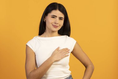 Turuncu arka planda gülümseyen genç bir kadın samimi, minnet, güven, bağlılık ve samimiyetini bir stüdyo resmine yansıtıyor.