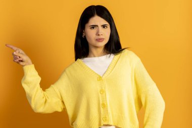 Sarı arka planda duran ciddi yüzlü ve çatık kaşlı bir kadın şüphe ve şüpheciliğini dile getirirken bir yandan da sola işaret ederek bir yön ya da nesneyi işaret ediyor.