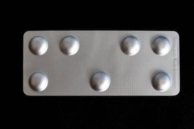 Siyah arka planda gümüş bir hap kutusu var. Hap kutusu dikdörtgen şeklinde ve içinde altı küçük yuvarlak hap var.