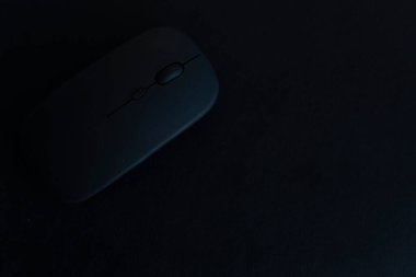Siyah bir bilgisayar faresi karanlık bir yüzeyde oturur. Fare küçük ve siyahtır ve bir masanın üzerine yerleştirilir. Görüntünün karamsar ve gizemli bir havası var.