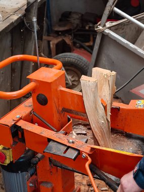 Güçlü turuncu hidrolik kütük ayırıcı kullanan kişinin elleri büyük bir tahta parçasını daha küçük kütüklere bölerek kışın ısıtma ve enerji için yakacak odun hazırlıyor.