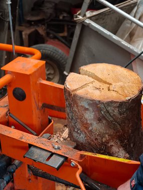 Büyük bir ağaç gövdesine güç veren turuncu bir kütük ayırıcıyı kapatın. Keresteyi ısıtma, kırsal ve kırsal kesimlerdeki odun üretimi ve hazırlık faaliyetleri için yakacak odununa ayırın.