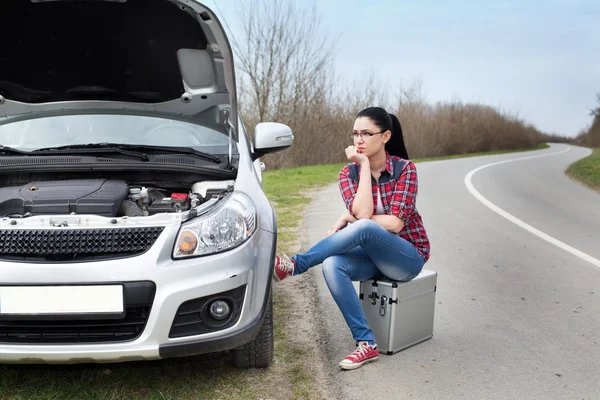 Chica sentada al lado del coche con capucha abierta — Foto de Stock