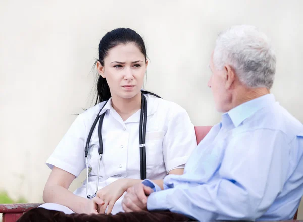 Jonge verpleegster met senior man op binnenplaats — Stockfoto