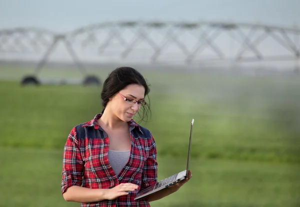 Farmer girl with laptop in front of irrigation system on field