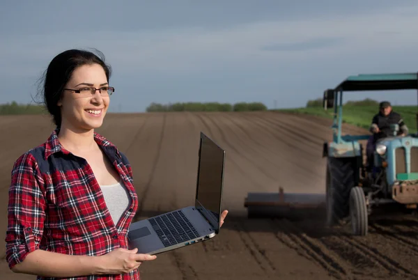 Bonde flicka med laptop i fältet med traktor — Stockfoto