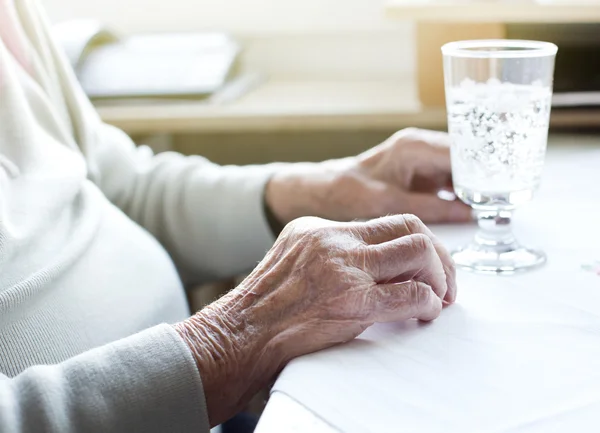 Las manos de la mujer mayor con un vaso de agua — Foto de Stock