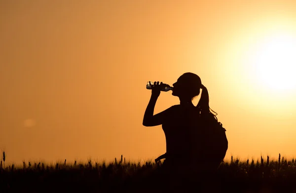 Žena pitnou vodu z láhve při západu slunce — Stock fotografie