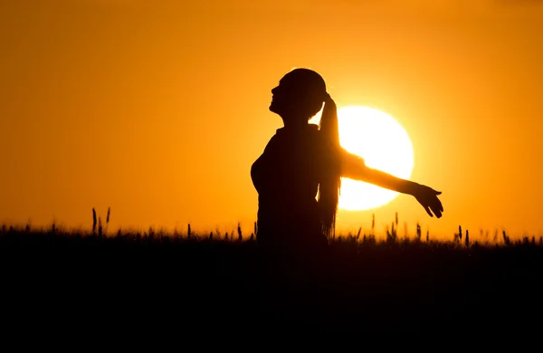 Silhueta de menina com as mãos levantadas ao pôr do sol — Fotografia de Stock