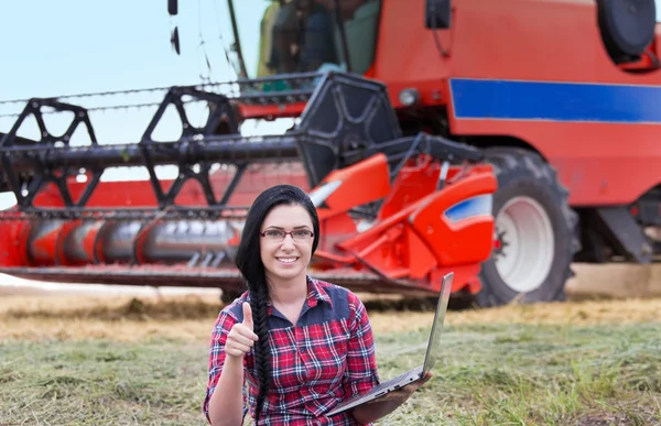 Chica agricultor con ordenador portátil y cosechadora — Foto de Stock