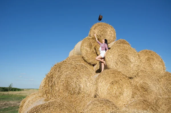 Girl throwing hat on straw bale — Stock Photo, Image