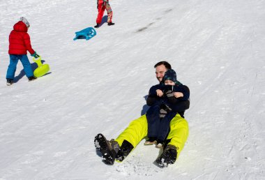 Baba ve oğul güneşli bir günde dağ yamacında kayak yapıyorlar.