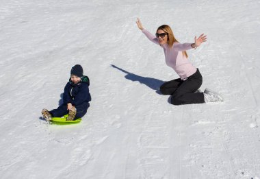 Anne ve oğlu güneşli bir günde kayak merkezinde dağ yamacında kayıyorlar.