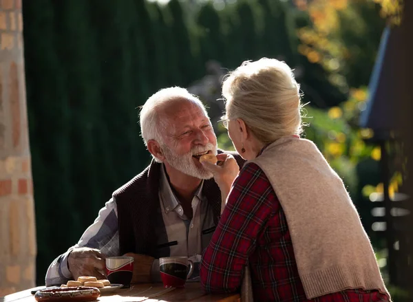 一对浪漫的老夫妇坐在花园的餐桌旁 喝咖啡 分享饼干 — 图库照片