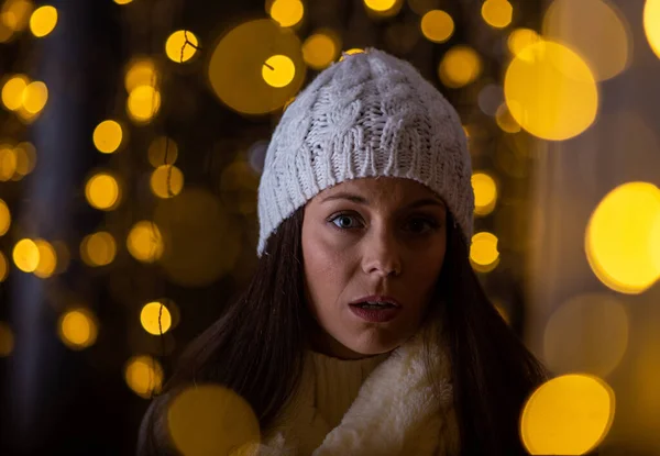 美しいです若いです女の子でコートとともに白い帽子歩く路上でクリスマスライト周りと店の窓を見て — ストック写真
