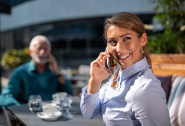 İki iş adamı, yaşlı bir adam ve genç bir kadın, kafede oturuyor, cep telefonuyla konuşuyor ve birini bekliyor.