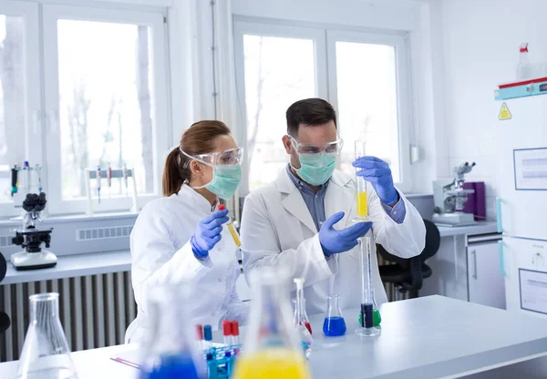 2人の生物学者が実験室でガラス瓶の中の化学物質を — ストック写真