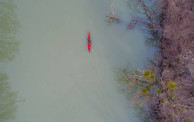 Kış günü donmuş nehirde kırmızı kanolu bir adamın en üst görüntüsü.
