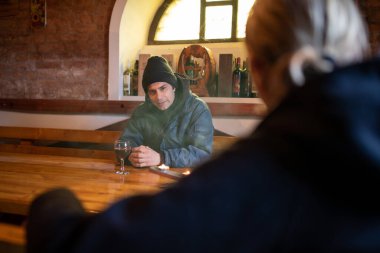 Şarap mahzeninde kırmızı şarap kadehiyle oturan iki adam.