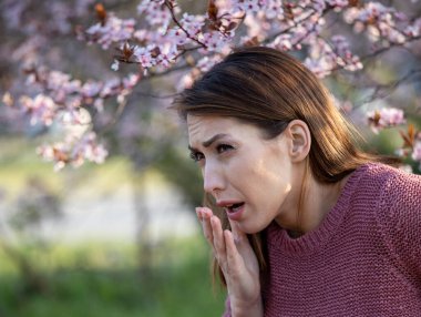 Çiçek açan ağacın önünde hapşıran güzel bir genç kadın. Bahar alerjisi saldırısı konsepti