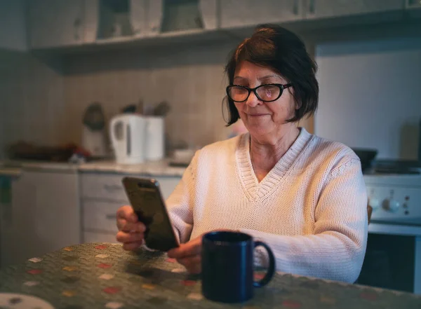 Leende Äldre Kvinna Sitter Köket Och Surfar Internet Mobilen — Stockfoto