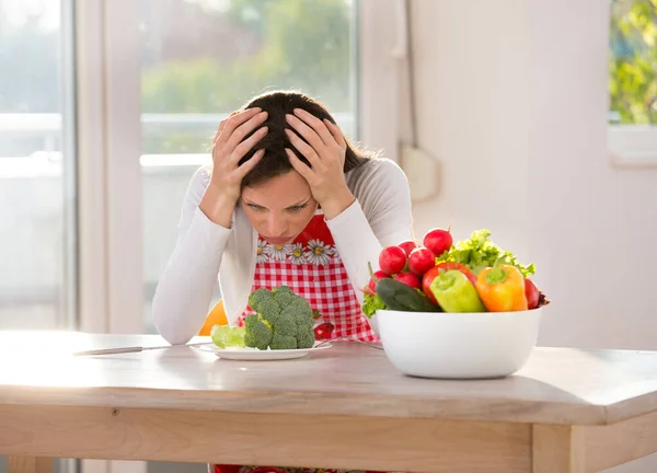 健康的な食べ物のためにかなりの女性が不幸な キッチンテーブルの上のプレートでブロッコリーの上の手で頭を保持 — ストック写真