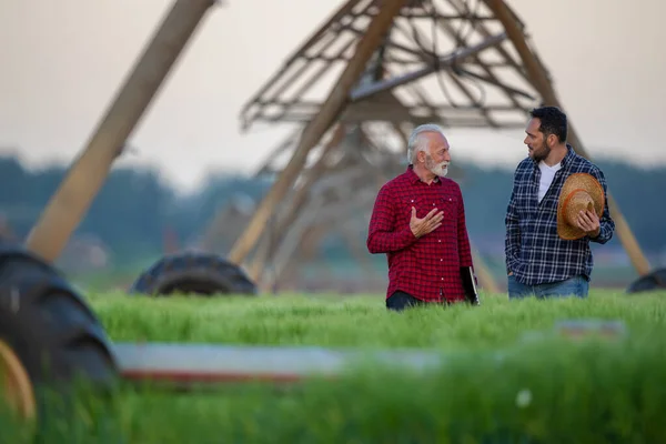 Two farmers standing in field talking showing center pivot irrigation system. Two men speaking explaining agriculture innovation.