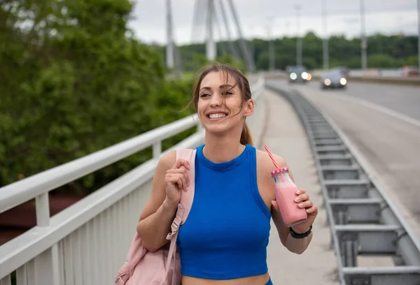 선수인 여자는 운동을 긴장을 미소짓는다 쉐이크 스무디를 마시며 다리를 — 스톡 사진
