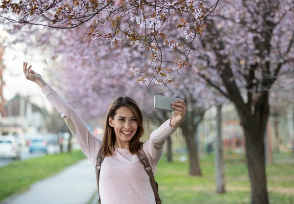 空中で腕を組んで自撮りしている魅力的な若い女性 春の花の木の公園を歩く女の子 — ストック写真