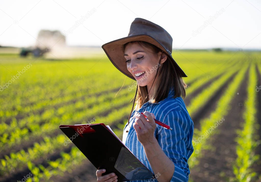 Portrait of female agronomist taking notes on growth of corn. Young farmer standing in field smiling satisfied. 
