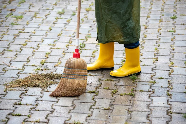 Kobieta Gumowych Butach Płaszczem Przeciwdeszczowym Zamiatanie Miotłą Betonowych Blokach Zewnątrz — Zdjęcie stockowe