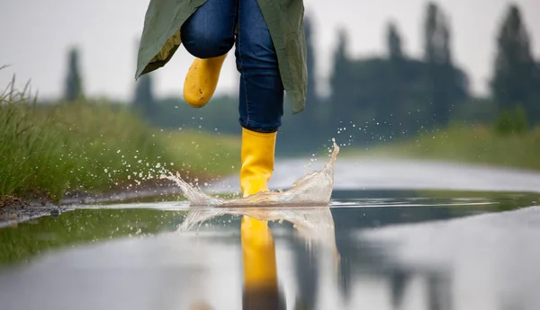 Close up of farmer\'s legs in yellow gumboots and green raincoat running on puddles after rain in field