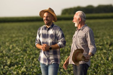 Handsome young farmer wearing straw hat laughing. Senior farmer holding straw hat in hand talking smiling. 
