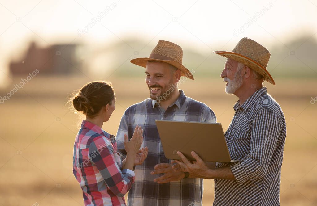 Young female farmer explaining talking to two male farmers. Elderly agronomist holding laptop discussing agriculture. Young male farmer listening smiling. 