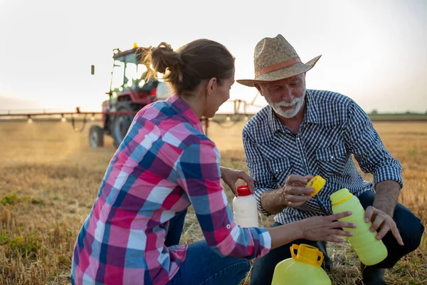 畑の噴霧器でトラクターの前のボトルに植物の世話のための化学物質を注ぐ農家の男性と女性 — ストック写真